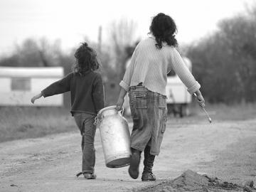 Kaksi lasta kantamassa maitotonkkaa hiekkatiellä